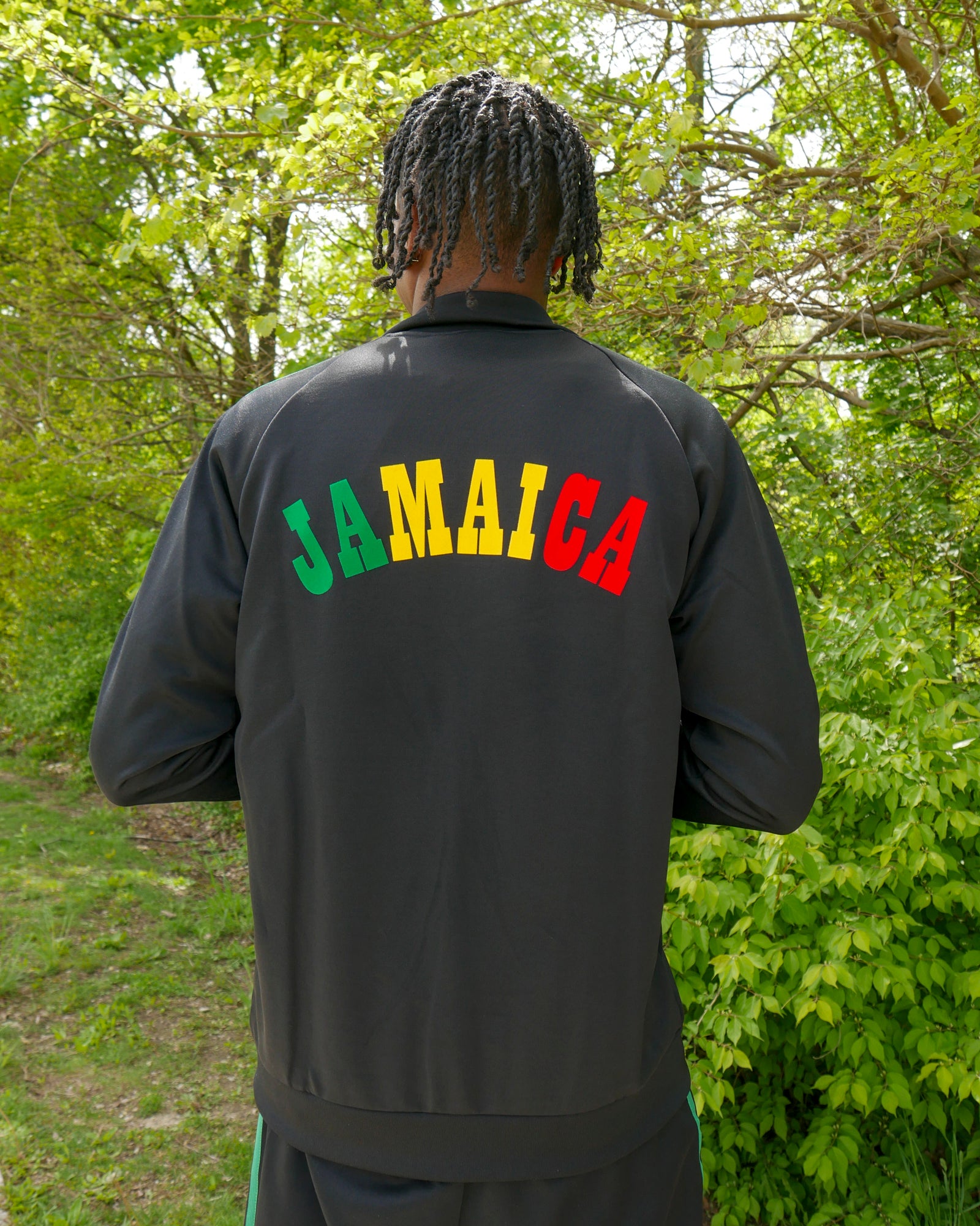 Person wearing a black jacket with 'JAMAICA' in colorful letters outdoors.