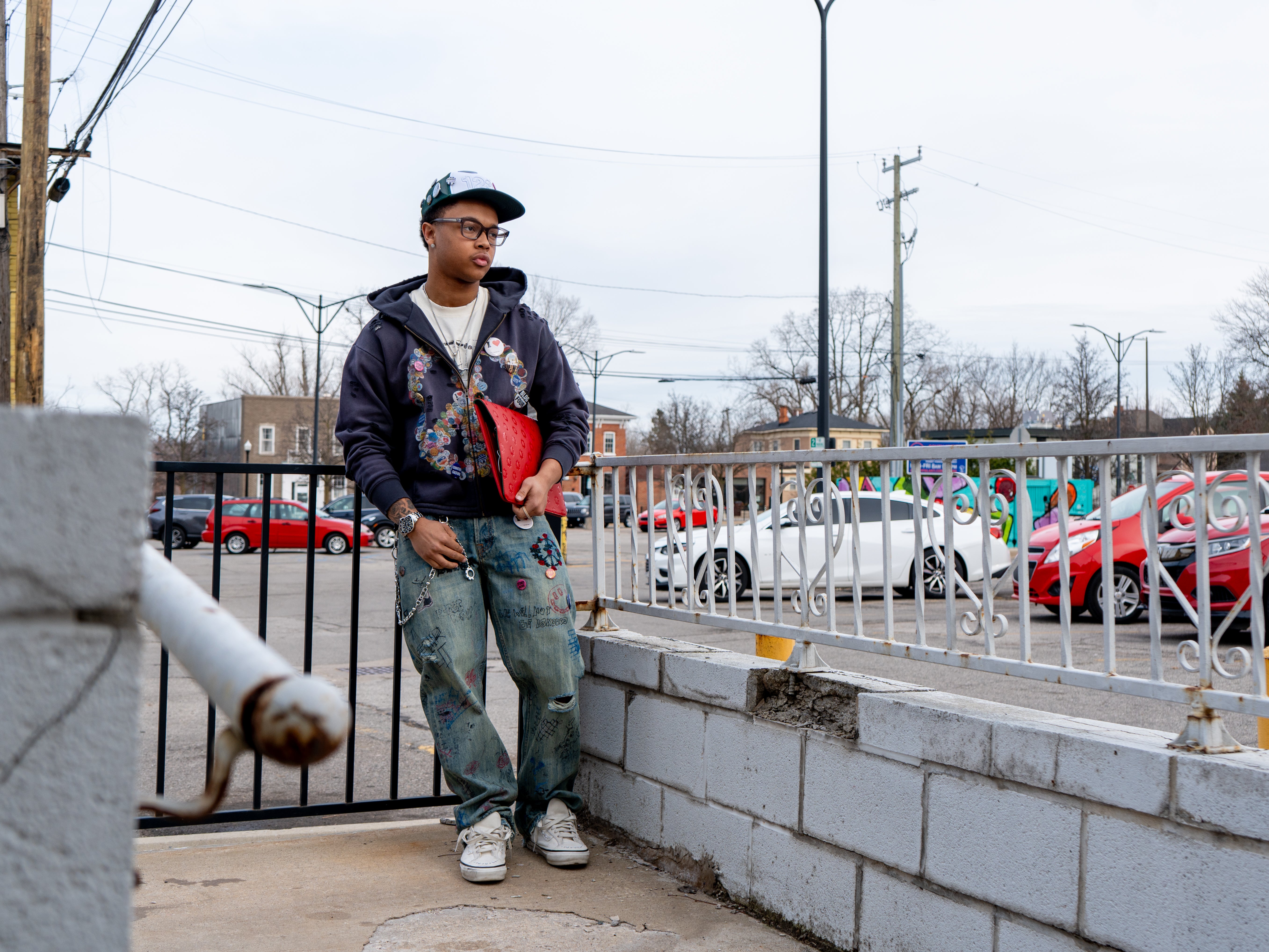 Person standing on a sidewalk with cars and a fence in the background