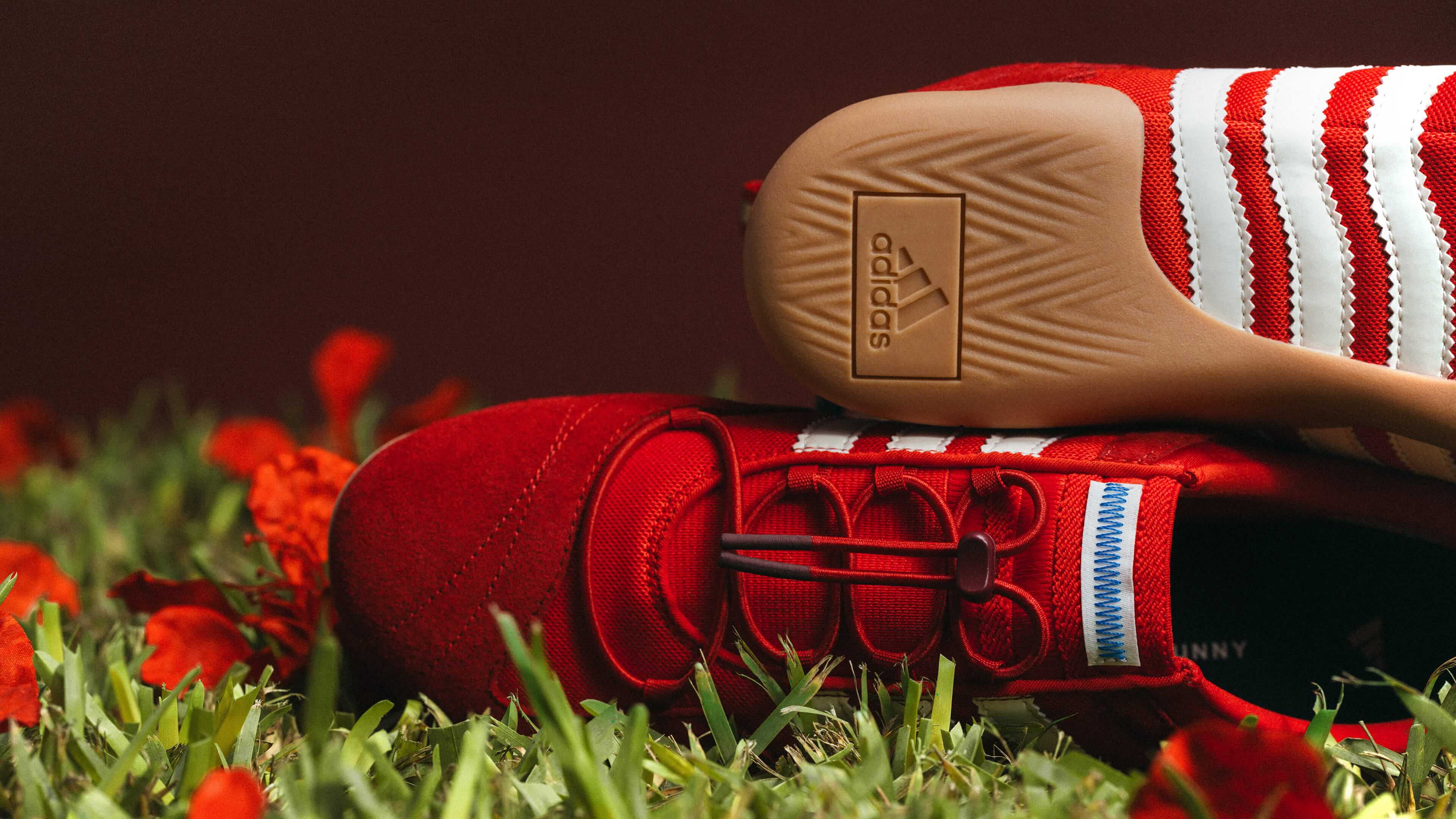 Red Adidas shoes with white stripes on grass
